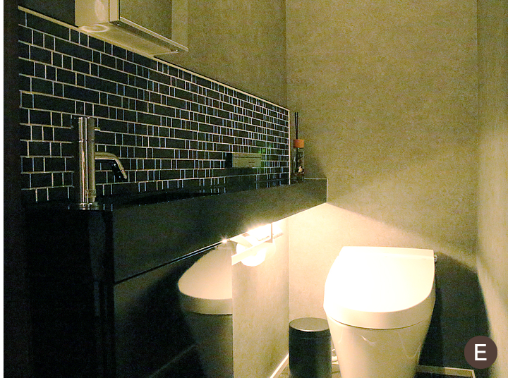１階のトイレ。床を照らす間接照明に、モルタル調のクロス、ブラックの手洗いカウンターで、洗練されたデザインに。タイルは、名古屋モザイクのオルモナ。